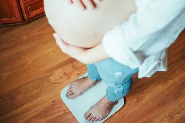Image of woman weighing herself and experiencing weight gain through pregnancy Port Glasgow